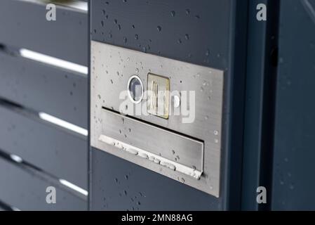 Ein modernes Videotelefon mit einem Briefkasten und einem drahtlosen Kartenleser, montiert in einem Anthrazit-Zaun, sichtbares Wicket, es regnet im Winter. Stockfoto