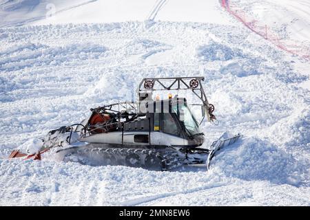 Ein Schneepflug in Aktion, der Schnee in den Bergen schaufelt. Ein Mann auf der Arbeit, der eine Schneefräse in den Bergen fährt. Arbeiten in Bergen mit Schnee Stockfoto