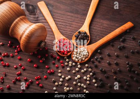Verschiedene Arten von Pfefferkörnern: Schwarz, weiß, rot und eine Pfeffermühle auf einem Holztisch. Stockfoto