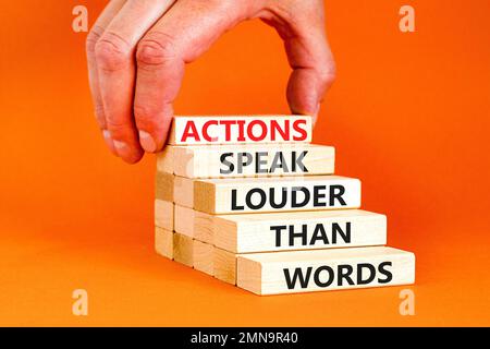 Das Symbol „Aktionen sprechen lautere Wörter“. Begriffe Taten sprechen lauter als Worte auf Holzblöcken. Schöner orangefarbener Tischhintergrund. Geschäftlich Stockfoto