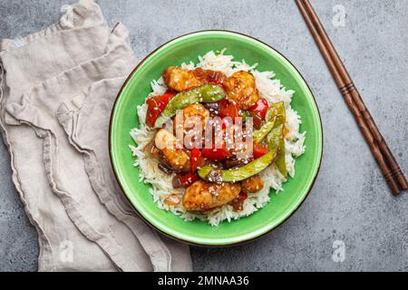 Asiatisches, süßes und sauriges, klebriges Hähnchen mit gebratenem Gemüse und Reis in einer Keramikschüssel mit Blick von oben, grauer rustikaler Steinhintergrund Stockfoto