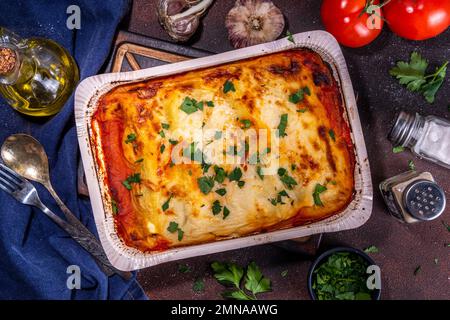 Hausgemachte Cannelloni-Pasta, großes Tablett mit gebackenen Cannelloni mit Hackfleisch mit Béchamel-Sauce, mit Kräutern in Zutaten auf dunklem Hintergrund Stockfoto