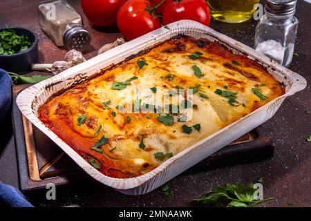 Hausgemachte Cannelloni-Pasta, großes Tablett mit gebackenen Cannelloni mit Hackfleisch mit Béchamel-Sauce, mit Kräutern in Zutaten auf dunklem Hintergrund Stockfoto