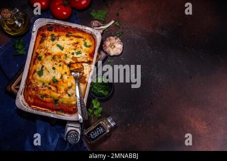 Hausgemachte Cannelloni-Pasta, großes Tablett mit gebackenen Cannelloni mit Hackfleisch mit Béchamel-Sauce, mit Kräutern in Zutaten auf dunklem Hintergrund Stockfoto