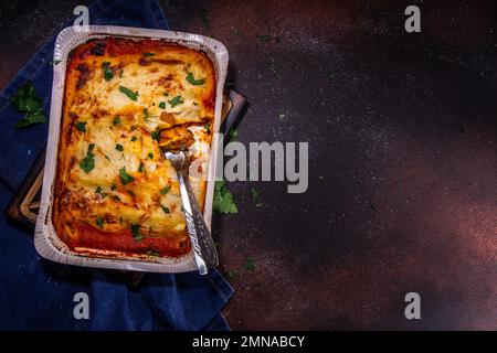 Hausgemachte Cannelloni-Pasta, großes Tablett mit gebackenen Cannelloni mit Hackfleisch mit Béchamel-Sauce, mit Kräutern in Zutaten auf dunklem Hintergrund Stockfoto