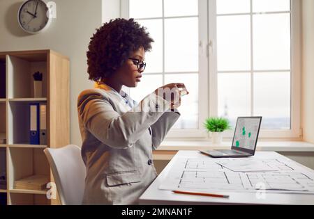 Architektin arbeitet im Büro und fotografiert den Bauplan auf dem Handy Stockfoto