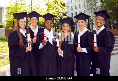 Gruppenporträt von glücklichen, vielfältigen Universitätsschülern in Kappen und Kitteln am Abschlusstag Stockfoto