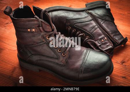 Dunkelbraune Stiefel aus altem Leder auf Holz Stockfoto