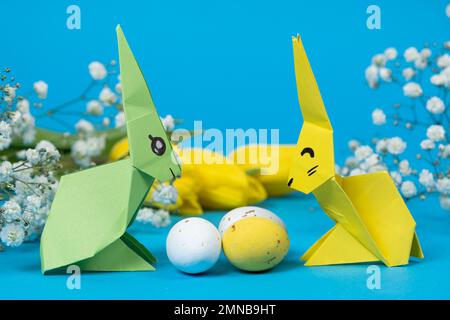 Zwei Origami-Hasen aus Papier und Ostereier auf blauem Hintergrund. Basteln Sie Ostern mit Ihren eigenen Händen Stockfoto