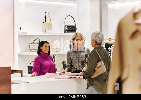 Zwei junge Verkäuferinnen, die mit einer Kundin in einer Boutique arbeiten Stockfoto