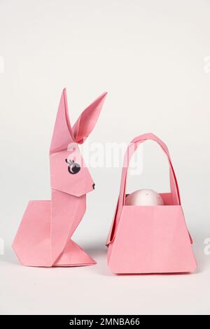 Ostern-Origami-Häschen und ein Korb mit Eiern auf weißem Hintergrund. Papierhandwerk, machen Sie es selbst. Stockfoto