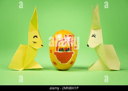 Oster-Origami - zwei Papierhasen und ein Ei mit grünem Hintergrund. Basteln für die Feiertage, machen Sie es selbst. Stockfoto