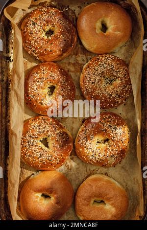 Vollformathintergrund mit frisch gebackenen Bagels auf Backpapier. Frische und knusprige Bagels mit Sesamsamen. Jüdisches Speisekonzept. Stockfoto