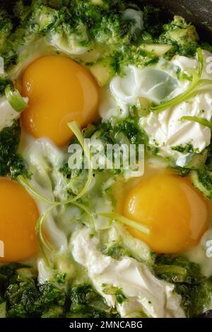 Nahaufnahme des grünen Shakshuka. Spiegeleier in einer gusseisernen Pfanne. Traditionelle jüdische Küche Stockfoto