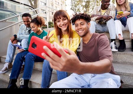 Eine Gruppe junger Freunde aus verschiedenen Ländern, die auf Treppen sitzen und Mobiltelefone benutzen. Stockfoto