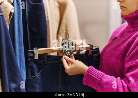 Nahaufnahme einer jungen Frau, die Jeans MIT EINEM VERKAUFSSCHILD in einem Einkaufszentrum anklebt, Kopierraum Stockfoto