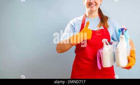 Frau in Handschuhen und Schürze, die einen Korb mit Schwamm und Reinigungsprodukten hält Stockfoto