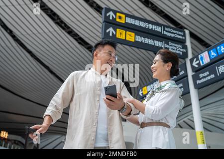Glückliches älteres Paar, das am Flughafen Mobiltelefone benutzt Stockfoto