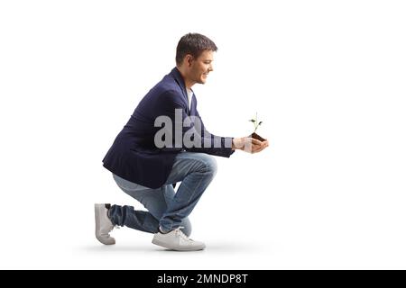 Ein Mann kniet und hält eine junge Pflanze und Erde in den Händen, isoliert auf weißem Hintergrund Stockfoto