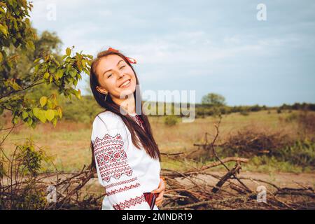 Foto einer lächelnden jungen Frau in einem ethnischen ukrainischen Hemd, die den wunderschönen und friedlichen Wochenendausflug genießt Stockfoto