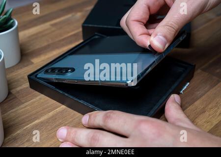 Samsung Galaxy Z Fold 4 in grau-grüner Farbe. Ein Mann packt das neue Handy aus. Stockfoto