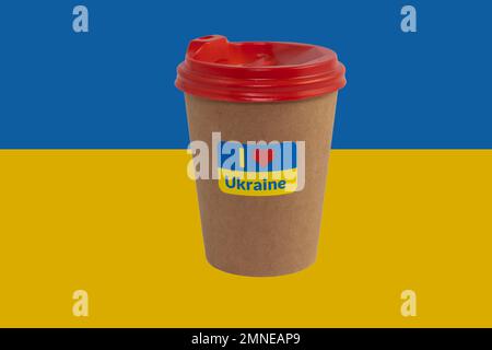 Einweg-Pappbecher Kaffee mit patriotischem Aufkleber „I love Ukraine“ isoliert auf dem Hintergrund der Nationalflagge der Ukraine (Nahaufnahme) Stockfoto