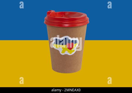 Einweg-Pappbecher Kaffee mit patriotischem Aufkleber „I love Ukraine“ isoliert auf dem Hintergrund der Nationalflagge der Ukraine (Nahaufnahme) Stockfoto