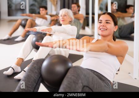 Menschen unterschiedlichen Alters, die Pilates mit Ball im Gruppenkurs im Yoga-Studio üben Stockfoto