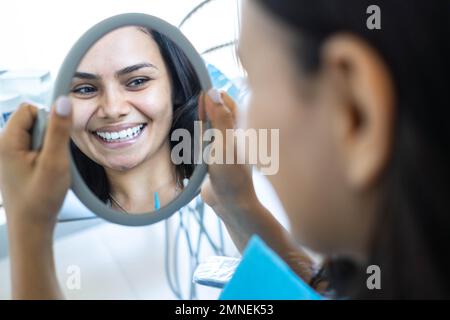 Reflexion einer schönen Frau, die in den Spiegel in der Zahnarztpraxis schaut. Stockfoto