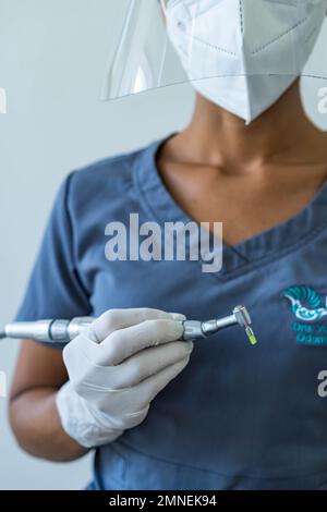 Zahnarzthand mit Handschuhen bei der Arbeit mit dem Zahnbohrer in der zahnärztlichen Praxis. Nahaufnahme, selektiver Fokus. Stockfoto