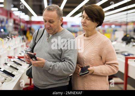 Ehefrau und Ehemann mittleren Alters pflücken neues Smartphone im Elektronikgeschäft Stockfoto