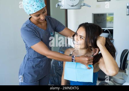 Schöne junge Frau in der Zahnarztpraxis, die lächelt und ihren Kieferorthopäden ansieht. Stockfoto