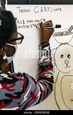 Ein Schüler schreibt während des 2022. Jugendaustauschprogramms in Camp Lester Middle School in Camp Lester, Okinawa, Japan, am 2. Oktober 2022 auf einem Whiteboard. Das Programm wurde vom Ministerium für auswärtige Angelegenheiten und dem Ministerium für Verteidigungsbildung organisiert und ermöglichte Teilnehmern aus Japan und den USA, gesunde Kommunikationsfähigkeiten zu üben und an Aktivitäten teilzunehmen, um mehr über die Kulturen der anderen zu erfahren. Die Studenten schufen kulturell gemeinsame Maskottchen, erhielten Auszeichnungen und etablierten dauerhafte Freundschaften. Stockfoto