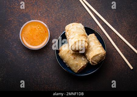 Chinesisches, thailändisches oder vietnamesisches traditionelles Gericht, frittierte Frühlingsrollen mit Füllung auf dem Teller mit süßer saurer Sauce auf rustikalem Betonhintergrund Stockfoto