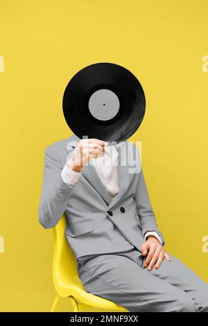 Ein Mann, der sein Gesicht mit Schallplatten verdeckt, während er ultimative graue Kleidung trägt. Hochauflösendes Foto Stockfoto