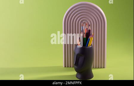 Die bunten Bleistifte werden in Vasenform gegen ein Grün gelegt. Stockfoto