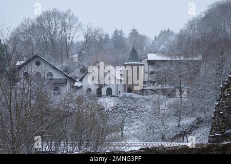 Falkenstein, Deutschland - 31. Januar 2021: Häuser und ein Turm auf einem Hügel, umgeben von Bäumen an einem nebligen, verschneiten, kalten Wintertag in Rheinland-Pfalz, G. Stockfoto