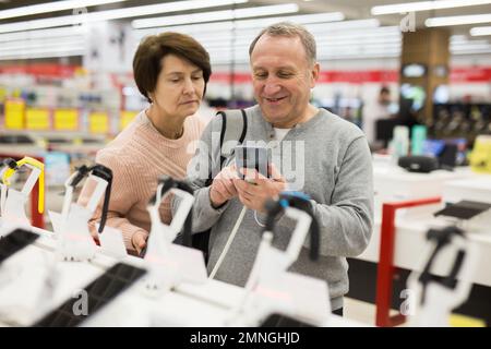 Reifer Mann und Frau, die sich für ein Smartphone im Elektronikgeschäft entscheiden Stockfoto