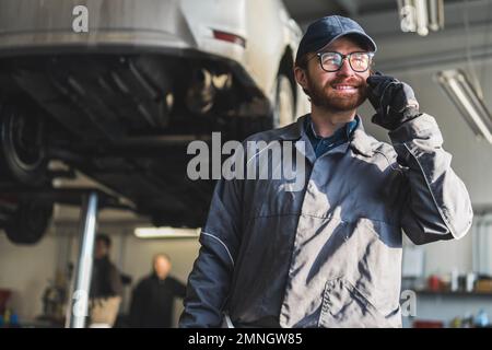 Automechaniker telefoniert in einer Autowerkstatt mit angehobenen Autos zur Reparatur. Hochwertige Fotos Stockfoto