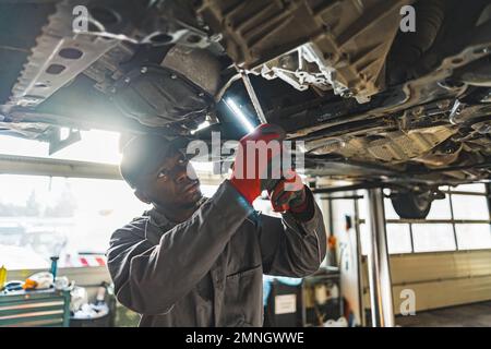 Erfahrener Mechaniker, der die Kupplung eines Fahrzeugs mit einer Taschenlampe in einer Autowerkstatt ersetzt. Hochwertige Fotos Stockfoto