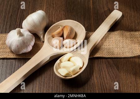 Knoblauch - Allium sativum; Holzlöffel mit Knoblauch; Foto auf dunklem Holzhintergrund. Stockfoto