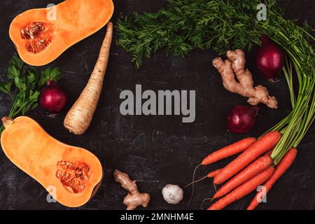 Rahmen aus Gemüse, Kürbis, Karotten, Ingwer, Zwiebeln, Pastinaken und Petersilie auf schwarzem Hintergrund. Gesunde vegane Rohkost. Draufsicht, flach liegend, Kopierbereich Stockfoto