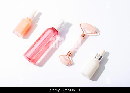 Pinkfarbene Kosmetikflaschen, Gesichtswalze auf weißem Hintergrund mit scharfen Schatten. Naturkosmetik, Hautpflegekonzept. Draufsicht Stockfoto