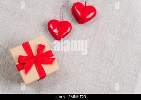 Zwei rote Spielzeugherzen und eine Geschenkbox auf Stoffhintergrund. Valentinstag-Konzept. Draufsicht, flach liegend, Kopierbereich Stockfoto