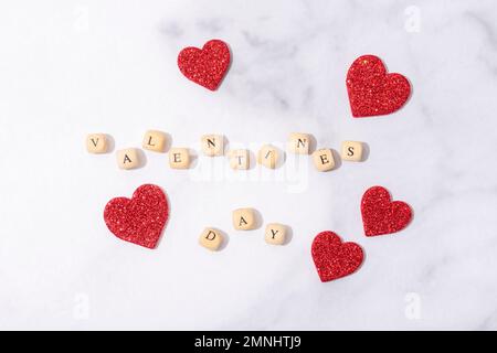 Holzblöcke mit Wörtern Valentinstag. Hölzerne Buchstabenblöcke auf Marmorhintergrund. Rote Herzen Dekoration. Draufsicht, flach liegend Stockfoto