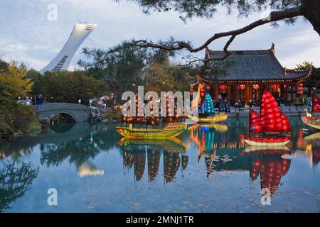 Beleuchtete chinesische Junks-Laternen und Friendship Hall-Pavillon am Dream Lake während der jährlichen Ausstellung Magic of Laternen im Chinesischen Garten in der Abenddämmerung. Stockfoto