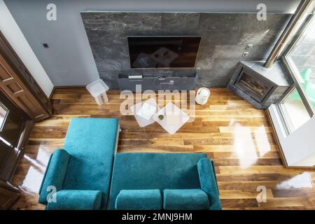 Wohnzimmer eines Hauses mit Kamin in einer Ecke mit Metallrohr, großer fernseher an der Wand vor einem Sofa mit grünem Samt Chaiselongue Stockfoto