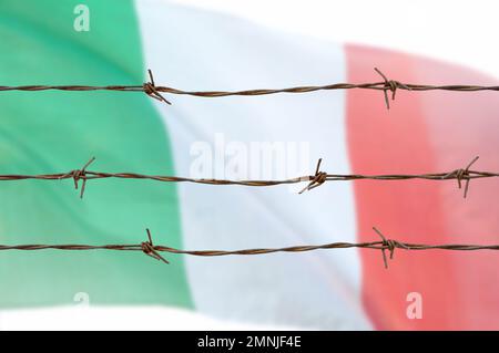Metallzaun mit Stacheldraht auf einer italienischen Flagge. Trennungskonzept, Grenzschutz. Soziale Fragen bei Flüchtlingen oder illegalen Einwanderern Stockfoto
