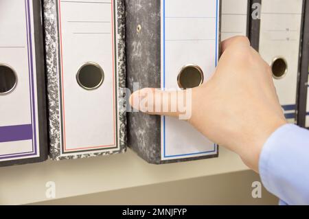 Die Hand eines Geschäftsmannes, der Akten in Regalen in einem Büro durchsucht Stockfoto