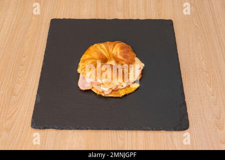 Französisches Croissant gefüllt mit truthahn und Käse auf einem quadratischen schwarzen Schiefer Stockfoto